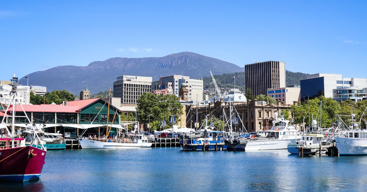 Harbor with boats, city buildings, and a mountain in the background under a clear blue sky.